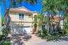 Stucco exterior featuring a clay tile roof, arched entryway, brick-paver driveway, and an attached two-car garage