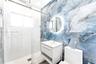 Large-format blue stone-finish wall tile, frameless glass shower enclosure with rain-style showerhead, floating vanity, circular backlit mirror, and w