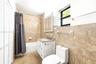 Bathroom featuring neutral-toned stone-finish wall and floor tiling with decorative border inlay, white vanity with integrated stone-finish countertop