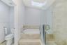 Built-in drop-in bathtub with stone-surround, frameless glass-enclosed shower, skylight, and neutral wall-mounted toilet