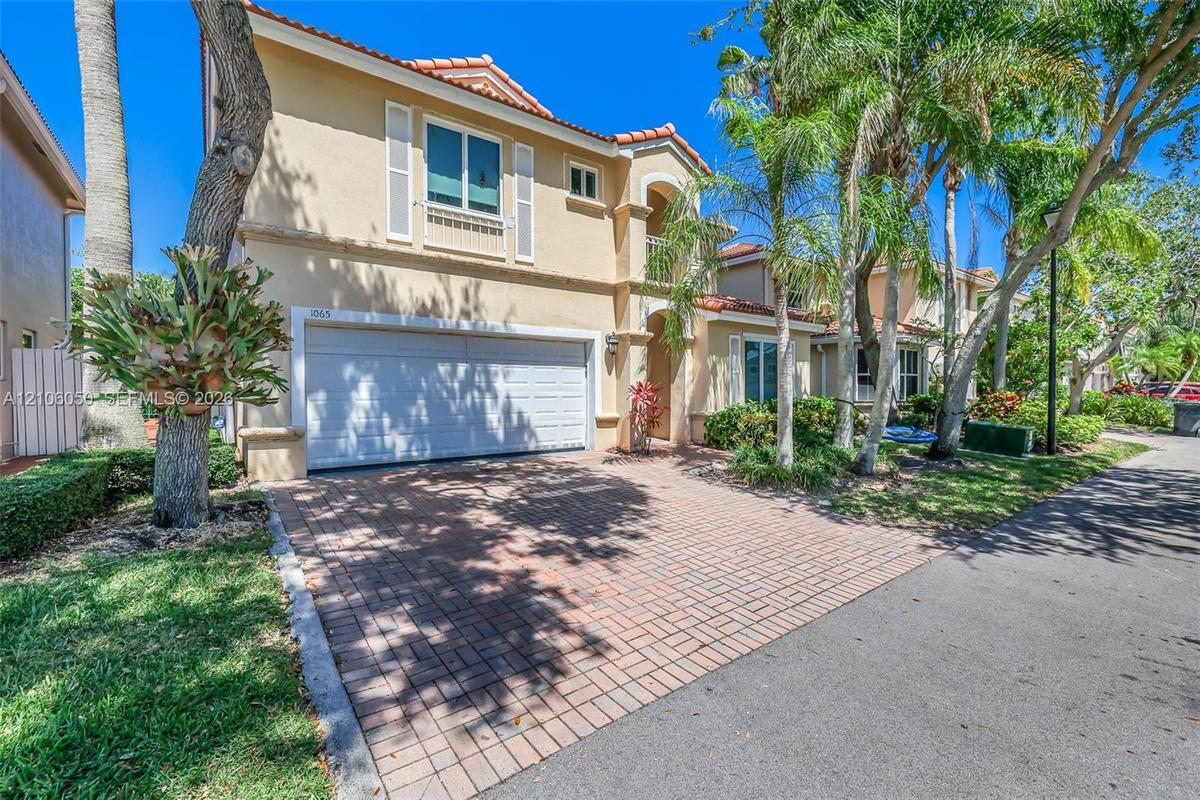 Stucco exterior residence featuring a clay tile roof, a paver driveway, an attached two-car garage, and established landscaping