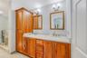 Double vanity featuring a light-toned stone countertop, wood cabinetry with integrated floor-to-ceiling storage, two wall-mounted mirrors with wood fr