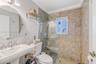 Pedestal sink with chrome faucet, oval wall-mounted mirror, and walk-in shower featuring glass enclosure and natural stone tile surround
