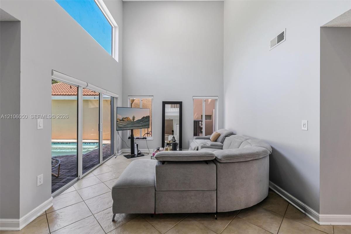 Double-height ceilings, ceramic tile flooring, expansive sliding glass doors, transom window, and dual vertical windows