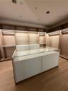 Custom Women’s primary closet , long mirror ,built-in wood cabinetry featuring integrated lighting and glass shelving, centered by a matching island w