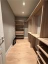Custom walk-in closet featuring light-toned wood-finish built-in shelving, integrated hanging rods, built-in storage drawers, and wood-finish flooring