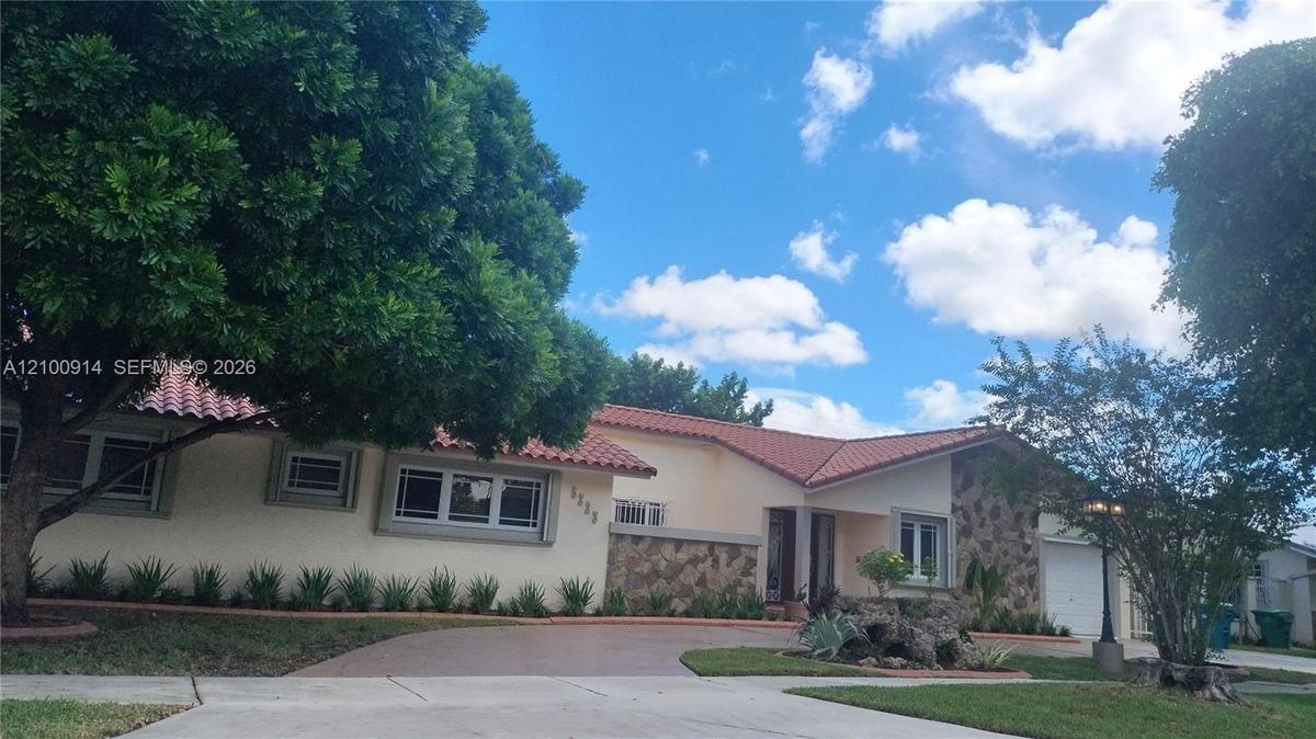 Covered rear patio featuring terracotta-style tile flooring, a built-in outdoor prep counter, and a light-colored stucco exterior