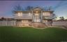 Elevated colonial-style home featuring a manicured lawn, vinyl siding exterior, brick foundation detailing, white vinyl fencing, and illuminated front