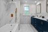 Stunningly renovated full bathroom showcasing floor-to-ceiling marble-inspired tile, a sleek double vanity, and elegant brushed gold fixtures for a to