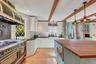 Kitchen featuring white cabinetry, double oven range, pendant lighting, range hood, and beam ceiling