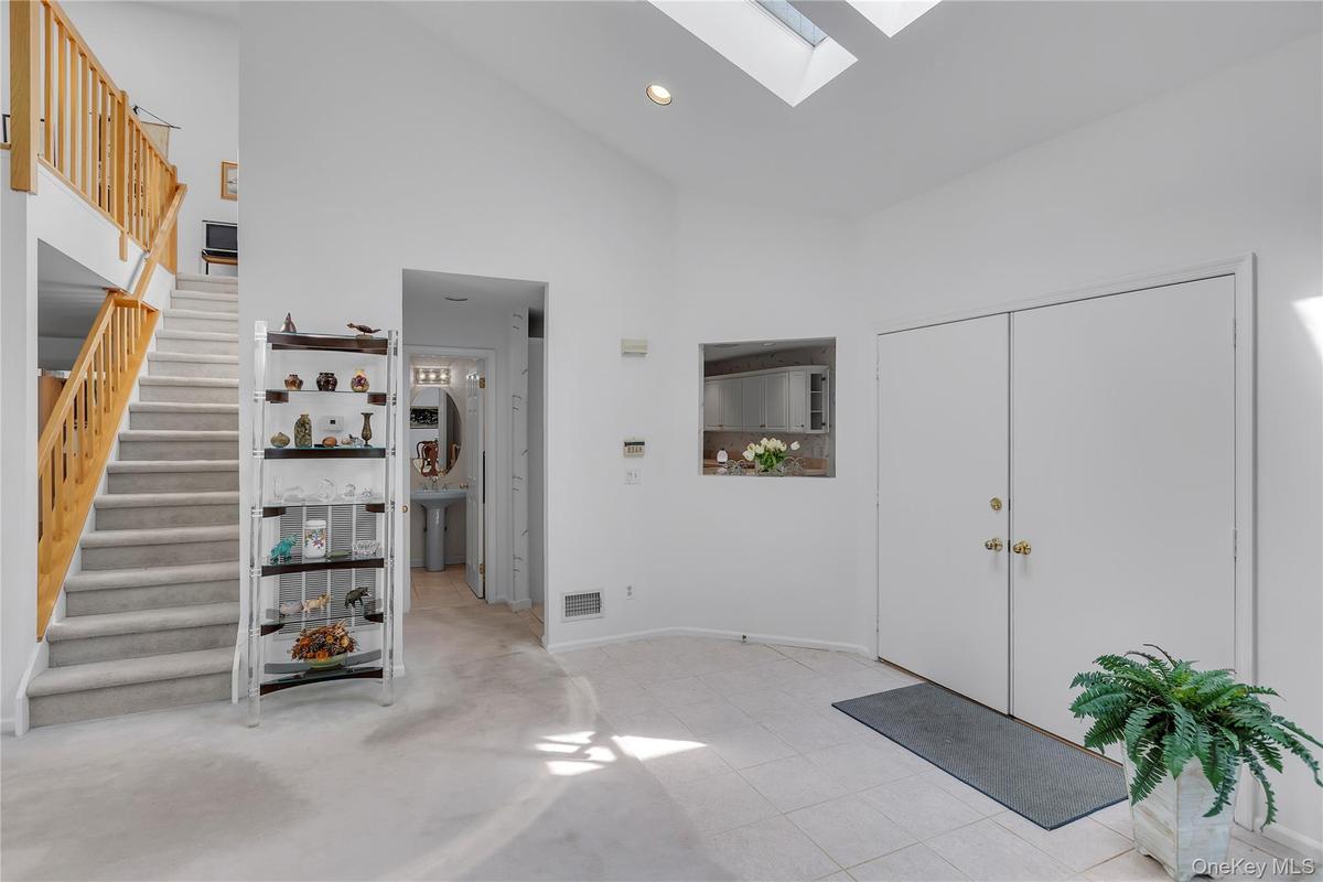 Two-story foyer featuring a vaulted ceiling with two skylights, a carpeted staircase with wood railings, and tile flooring at the entrance