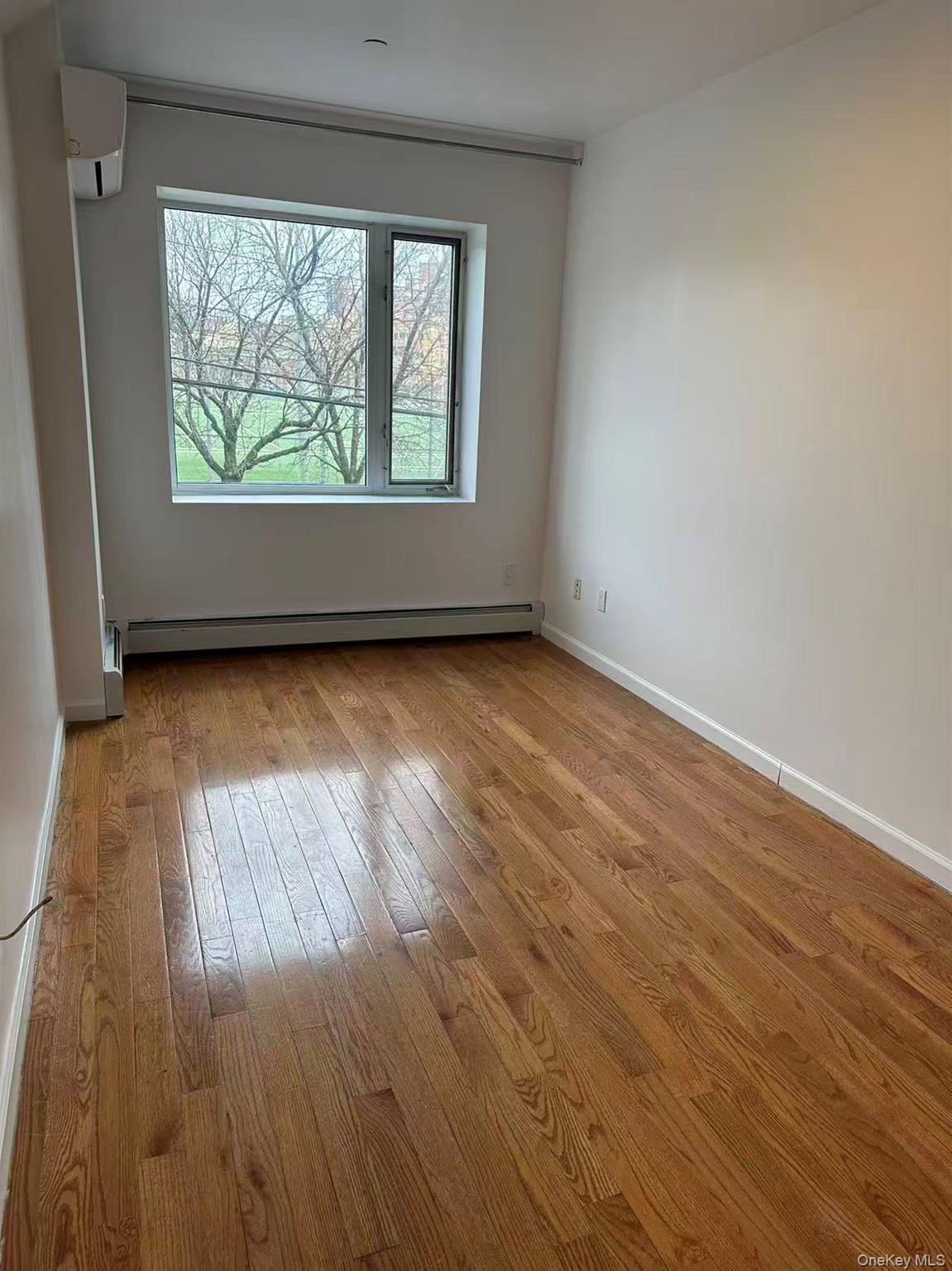 Spare room featuring light wood-type flooring, a wall mounted air conditioner, and a baseboard heating unit