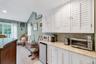 Galley area featuring white shaker-style cabinetry with louvered doors, a mosaic tile backsplash, and a granite-finish countertop
