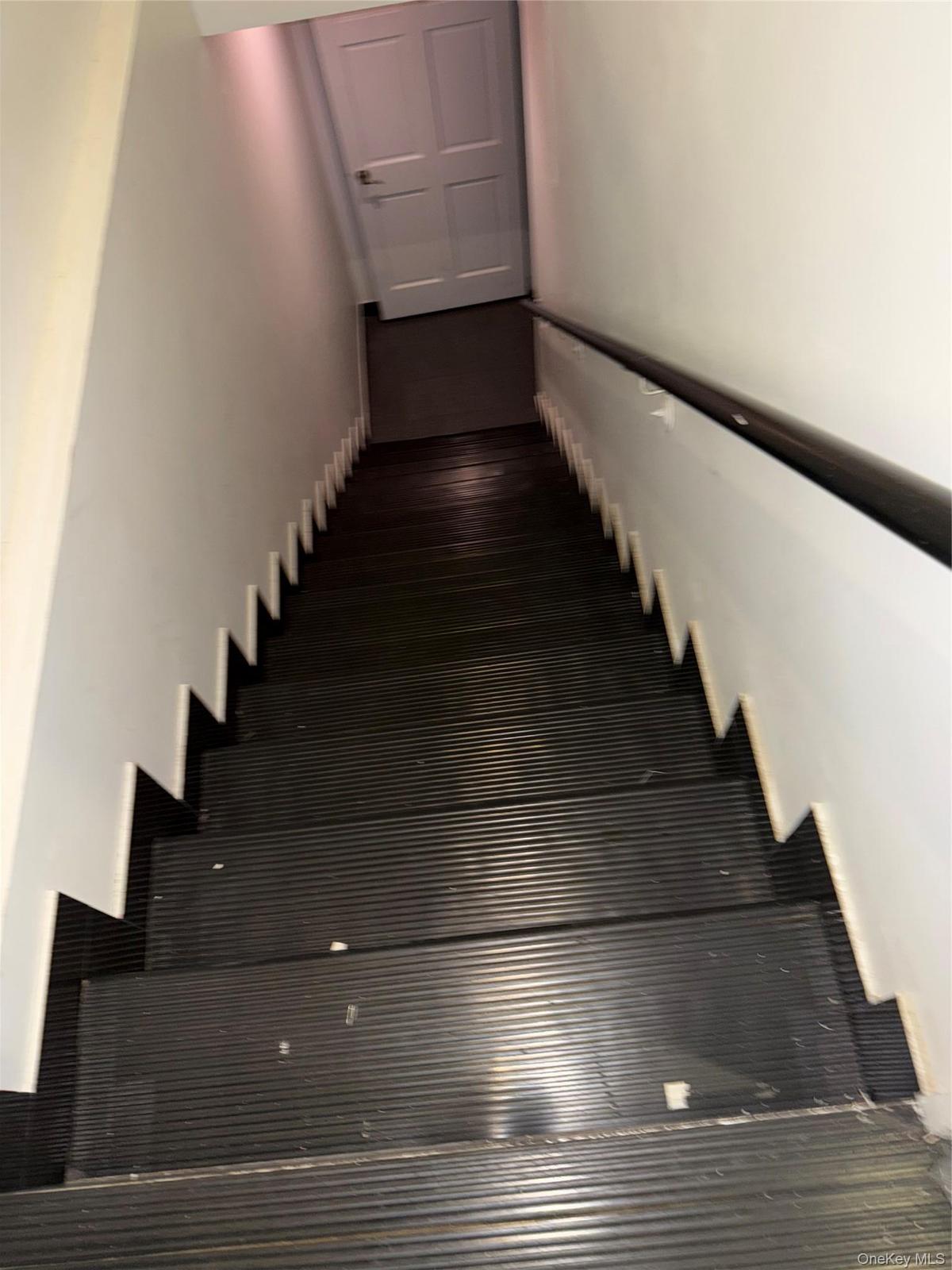 Staircase featuring dark tread covers, a contrasting white wall, and a black handrail