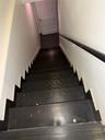 Staircase featuring dark tread covers, a contrasting white wall, and a black handrail