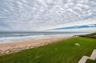 A lush green lawn frames wide ocean views and provides open space between the residence and the shoreline, ideal for outdoor lounging or play.