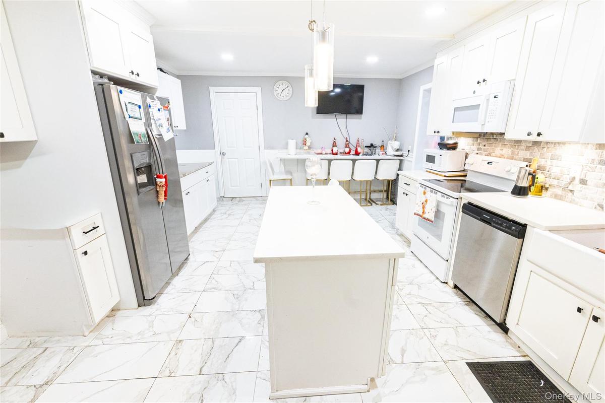 Kitchen with a kitchen island, stainless steel appliances, white cabinetry, hanging light fixtures, and crown molding