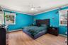 Spacious primary bedroom featuring vibrant turquoise walls, wood-finish flooring, and abundant natural light from dual windows