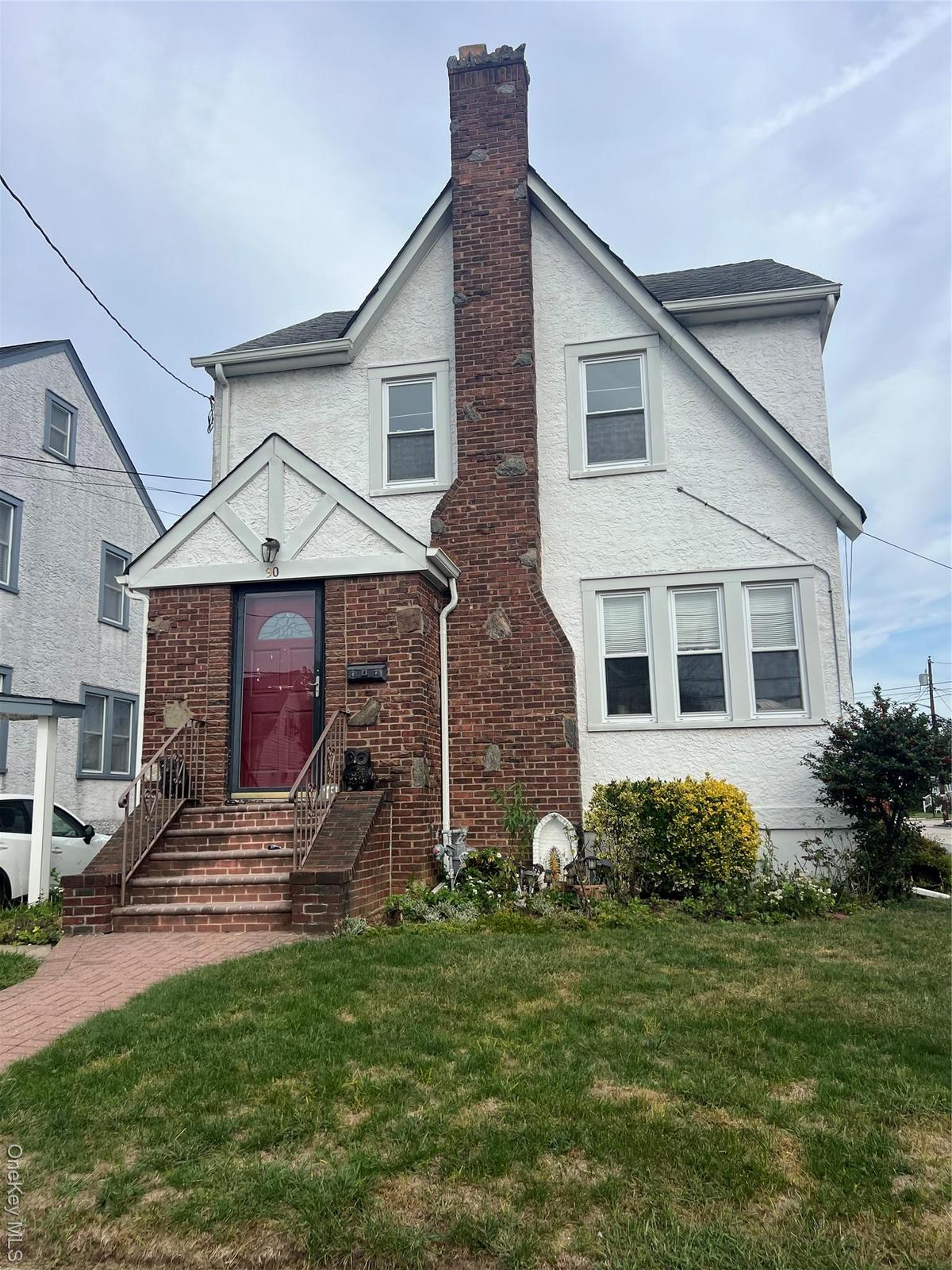 View of front facade with a front lawn, a chimney, and stucco siding