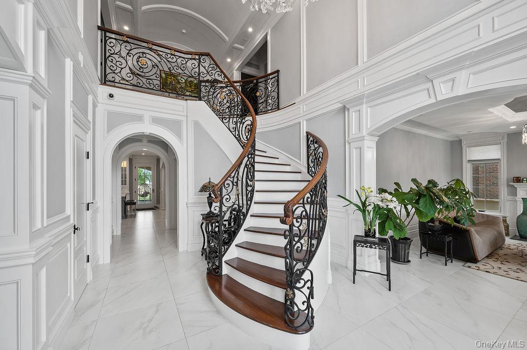 Entryway with arched walkways, light marble finish floors, a decorative wall, stairs, and recessed lighting