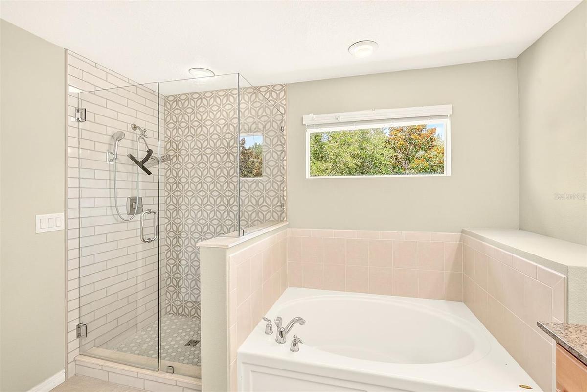 Primary en-suite bathroom featuring a large glass enclosed shower, large garden tub