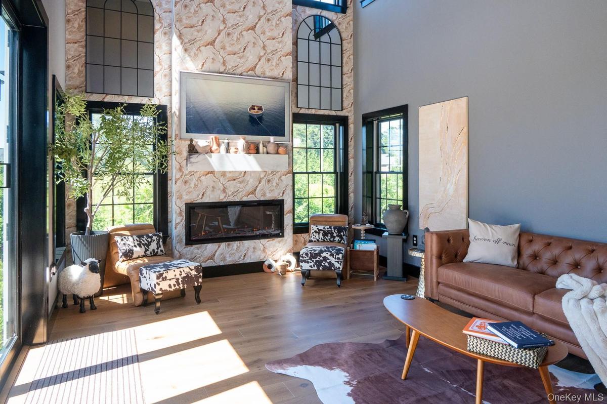 Living room with a glass covered fireplace, wood finished floors, and a high ceiling