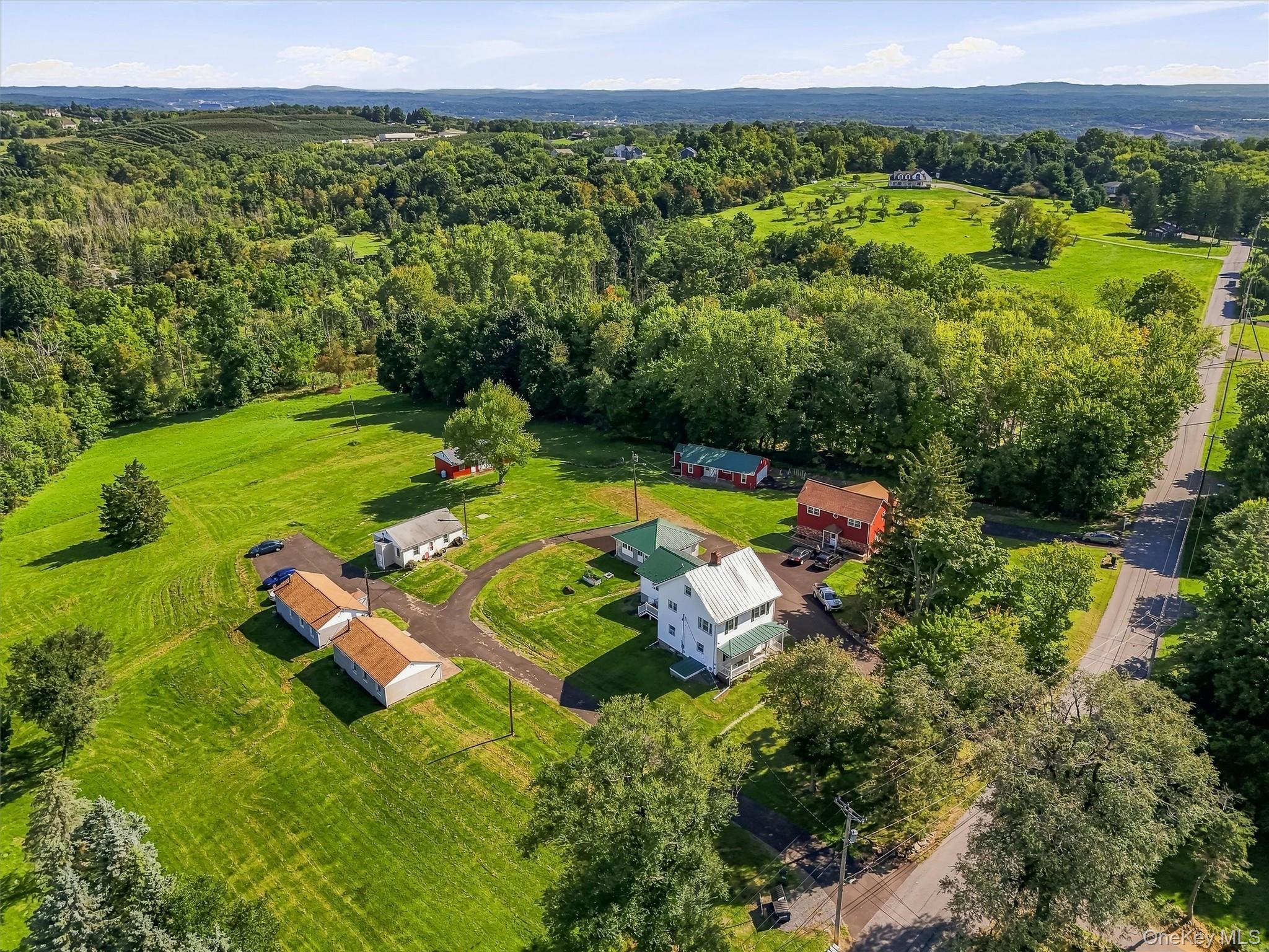 Expansive property featuring multiple structures, mature trees, open green spaces, and paved driveways