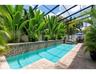 Pool area with waterfall feature, surrounded by a paver deck, outdoor shower and privacy screens, area behind pool enables large in ground plantings