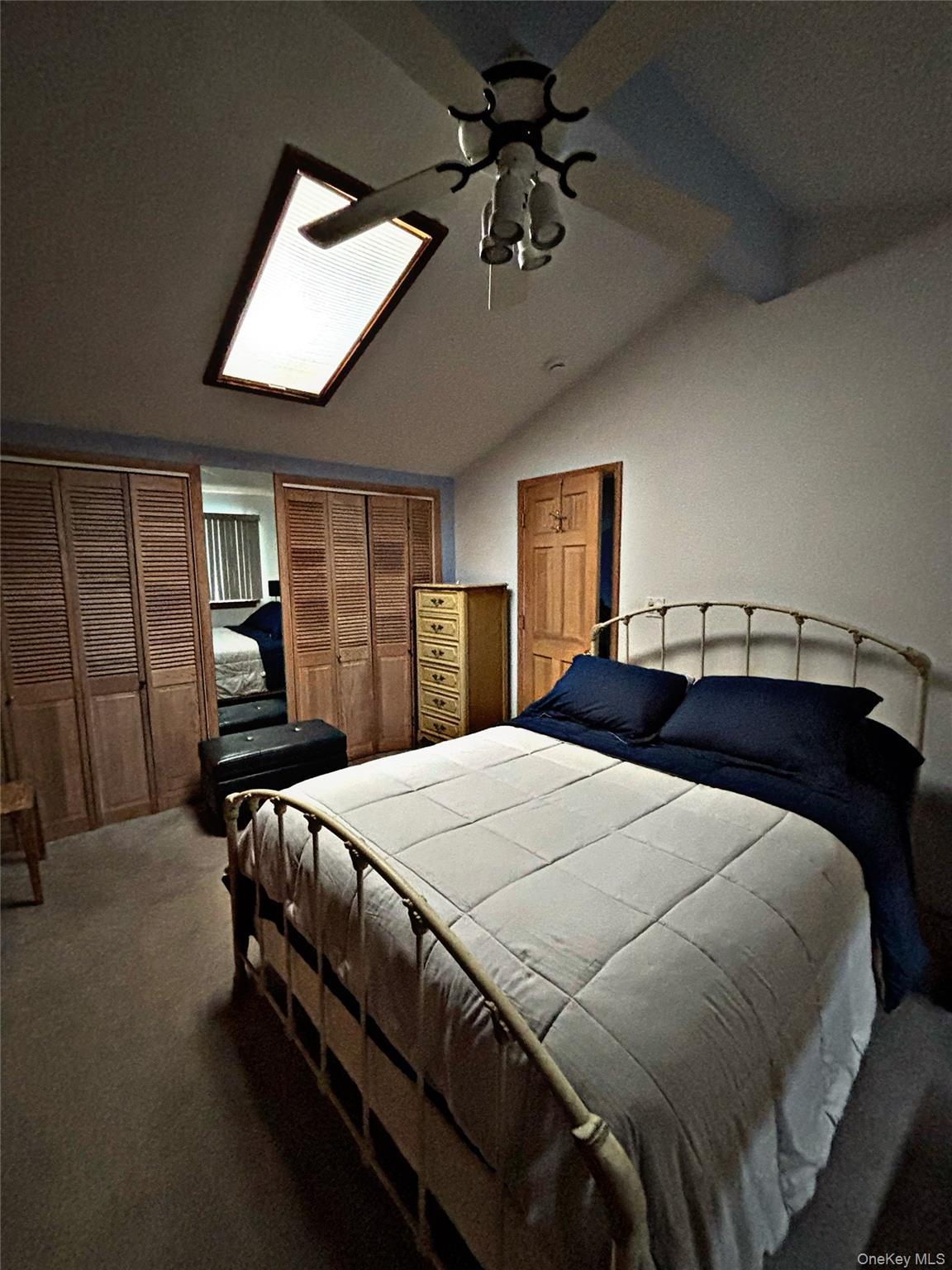 Bedroom featuring a vaulted ceiling with skylight, ceiling fan with light fixture, and wood louvered bifold closet doors