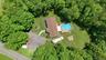 Expansive property featuring a central residence with a brown shingle roof, an oval above-ground pool with surrounding wood decking, and a large grass