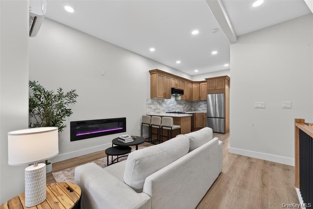 Open-concept living area featuring an electric fireplace, wood-finish flooring, recessed lighting, and a kitchen with wood cabinetry and stainless ste