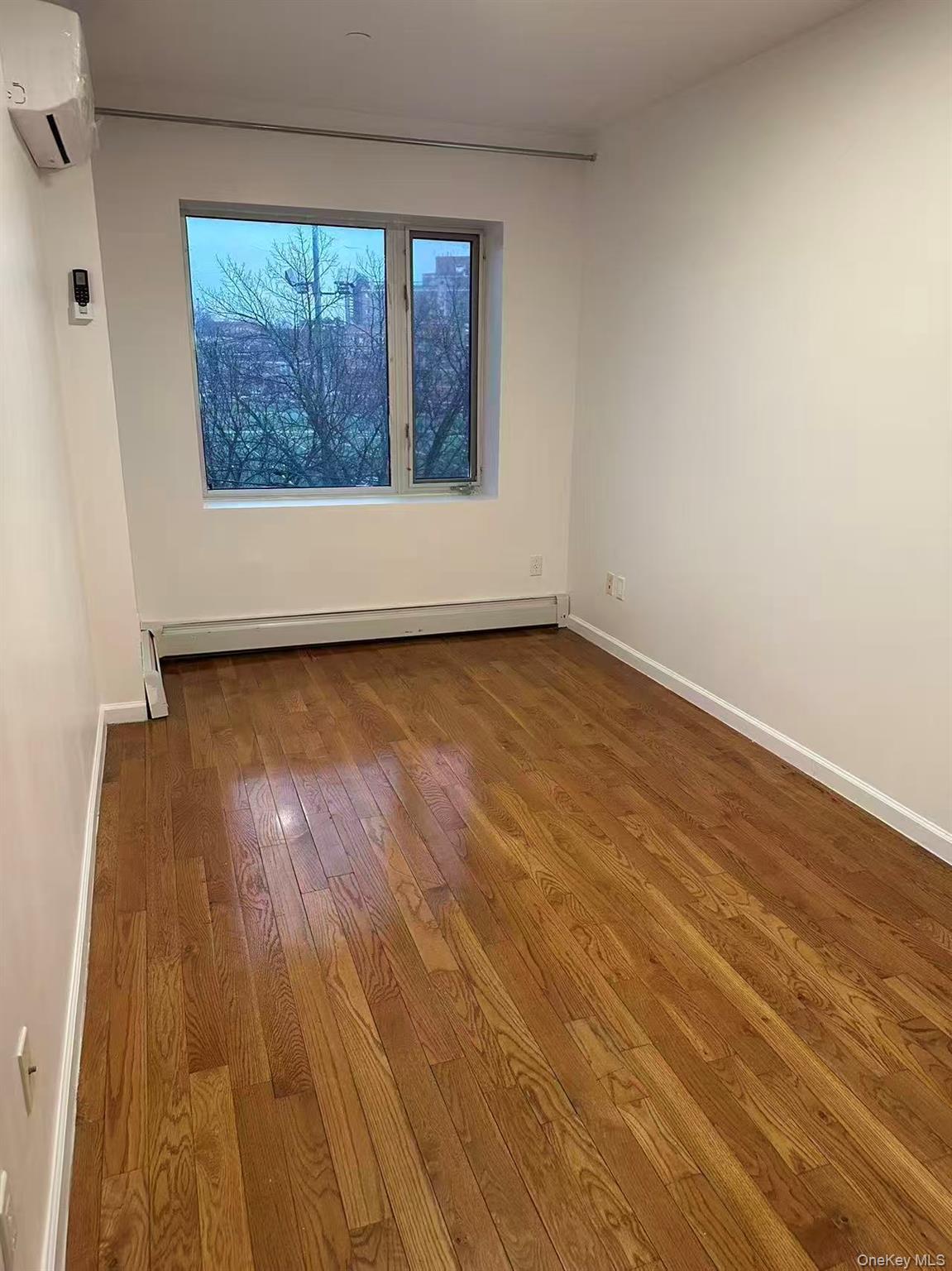 Empty room featuring wood-type flooring, a wall unit AC, and a baseboard heating unit