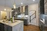 Kitchen with gray cabinetry, wall chimney exhaust hood, dark hardwood / wood-style flooring, an island with sink, and pendant lighting