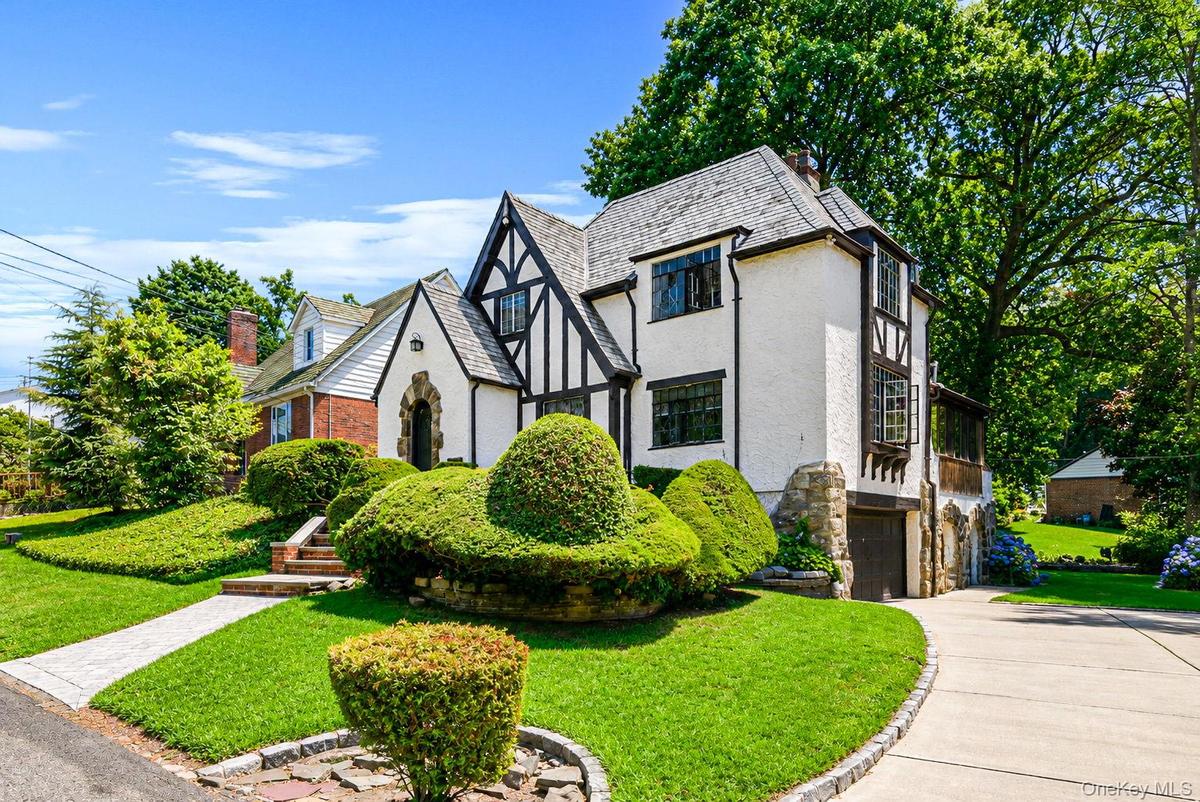 Tudor-style residence featuring a prominent front gable, stucco and half-timbering accents, a stone-clad foundation, and a slate-tile roof