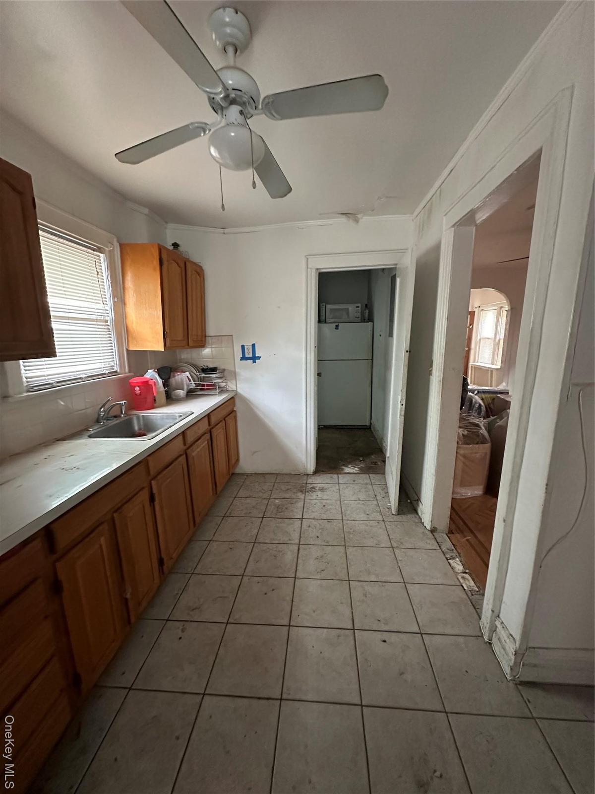 Kitchen featuring tasteful backsplash, light countertops, ceiling fan, light tile patterned floors, and brown cabinets