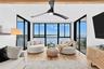 Living room with dual sliding-door balcony access, oversized swivel chairs, and wide open-water views.