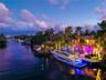 Aerial canal-level view at dusk featuring private deep-water dock, large motor yacht with underwater LED lighting, covered boat lift, illuminated wate