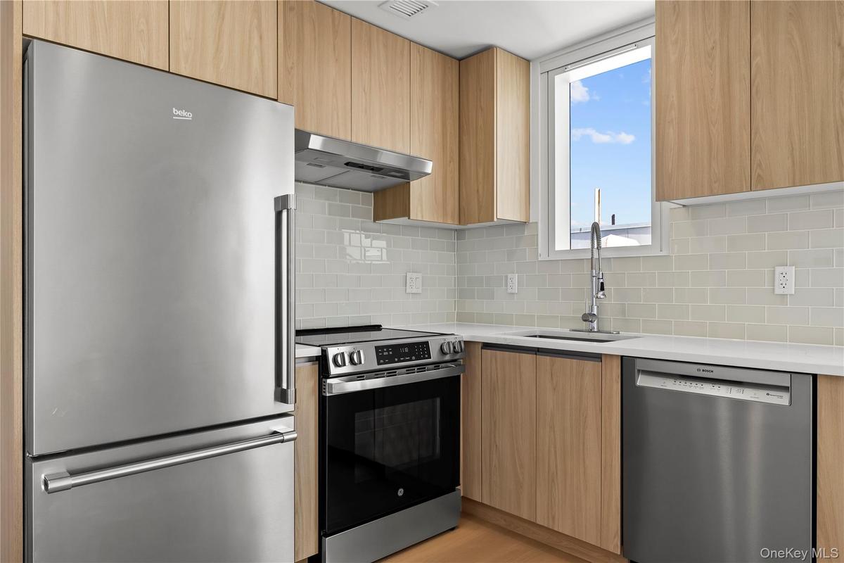 Kitchen featuring appliances with stainless steel finishes, modern cabinets, light stone countertops, and under cabinet range hood