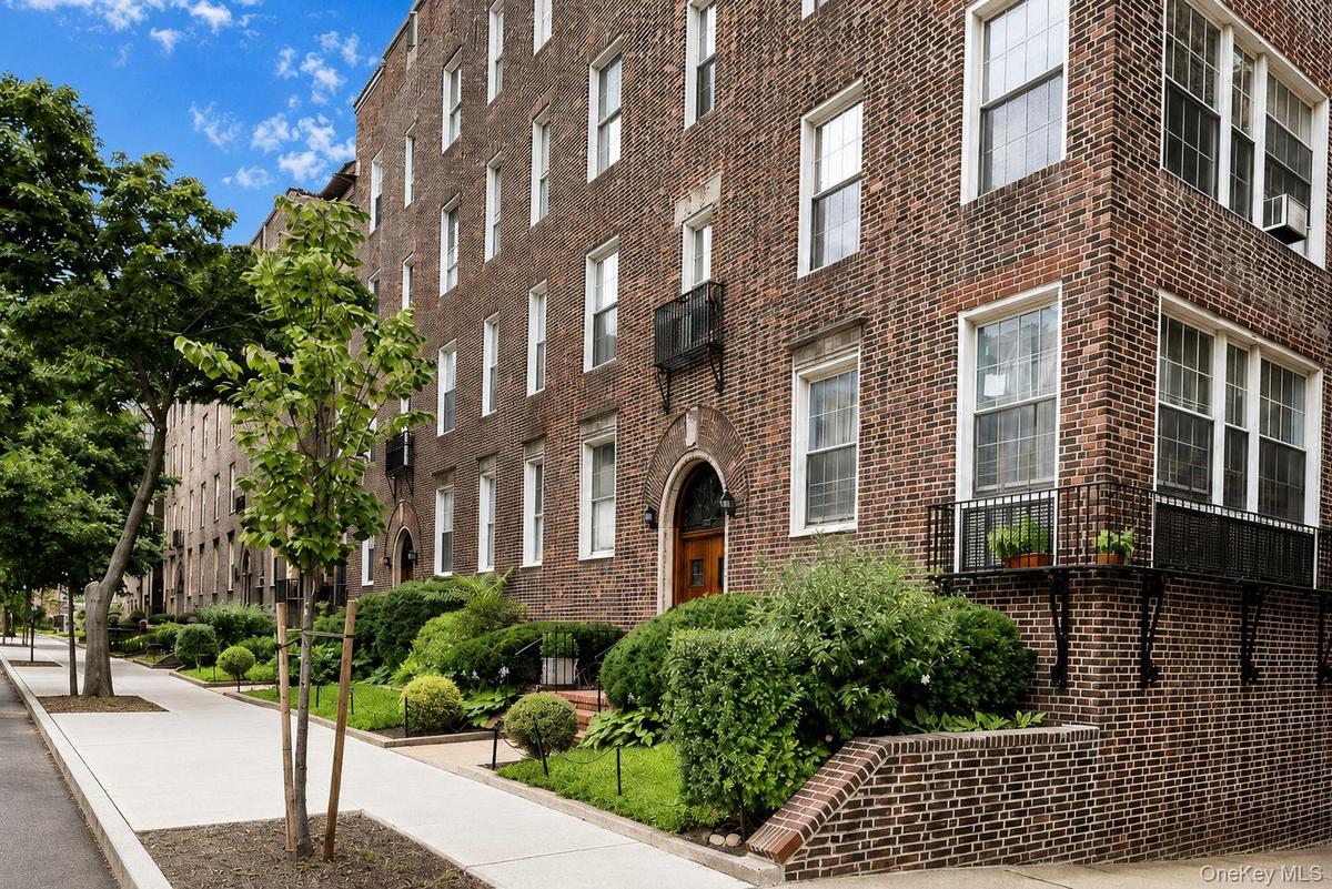 Brick exterior featuring multiple windows, established landscaping, and a sidewalk