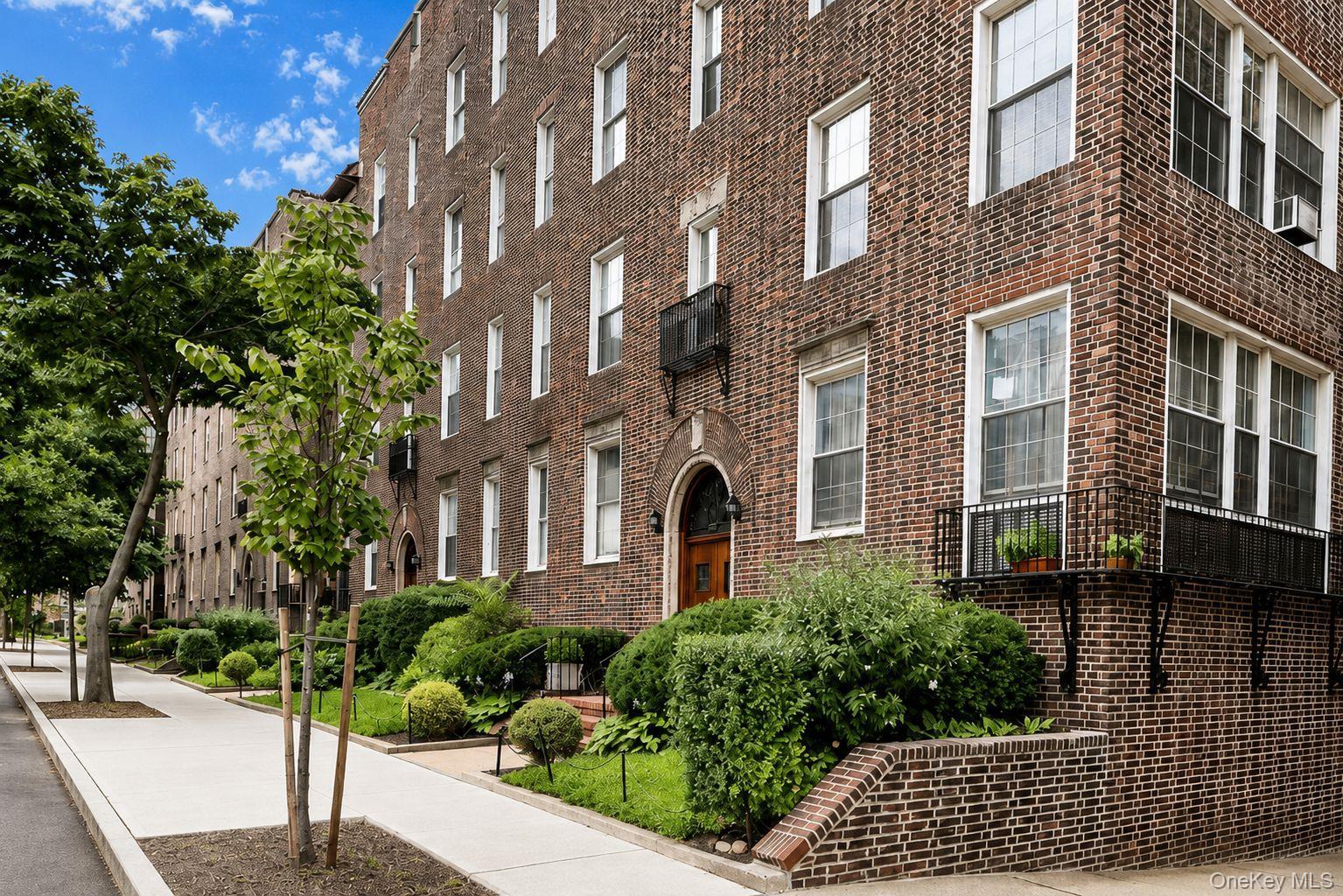Brick exterior featuring multiple windows, established landscaping, and a sidewalk