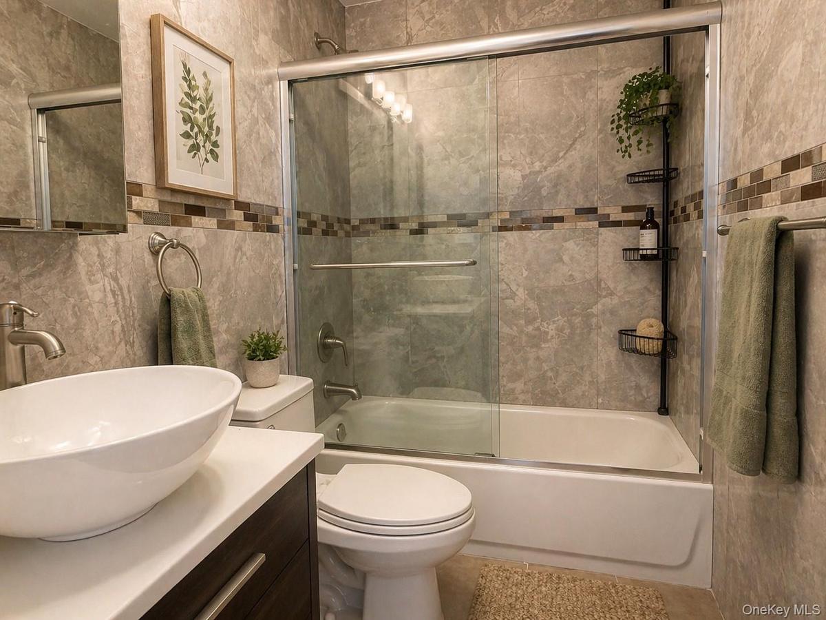 First Bathroom – Stylish full bathroom featuring floor-to-ceiling stone-style tile, a tub and shower combination with sliding glass enclosure, contemp