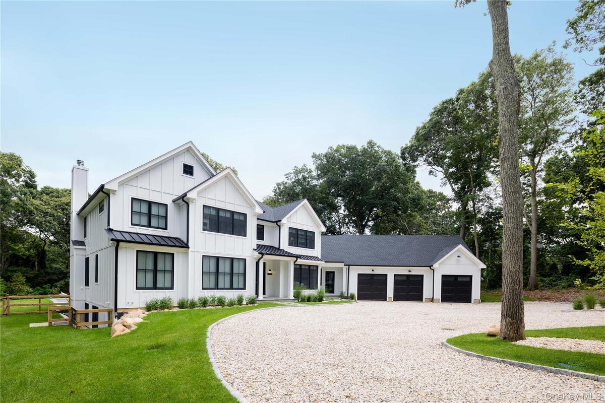 Modern farmhouse with gravel driveway, board and batten siding, an attached garage, a standing seam roof, and a chimney