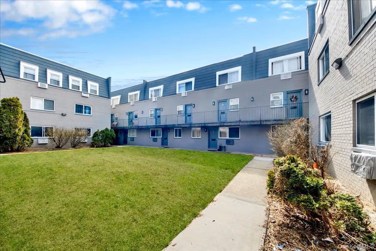 Courtyard-facing multi-unit residential building featuring a manicured lawn, concrete walkways, and established shrubbery