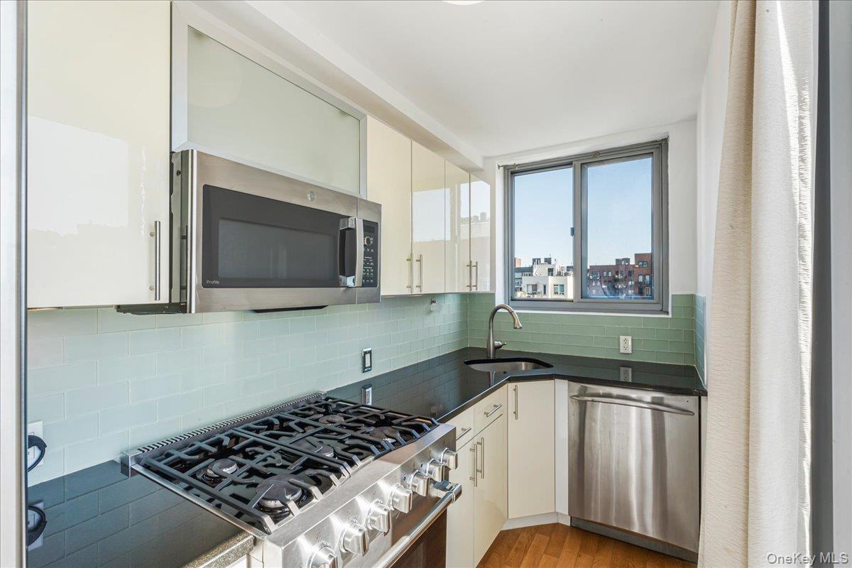 Kitchen with appliances with stainless steel finishes, tasteful backsplash, white cabinetry, light wood-style flooring, and dark stone counters