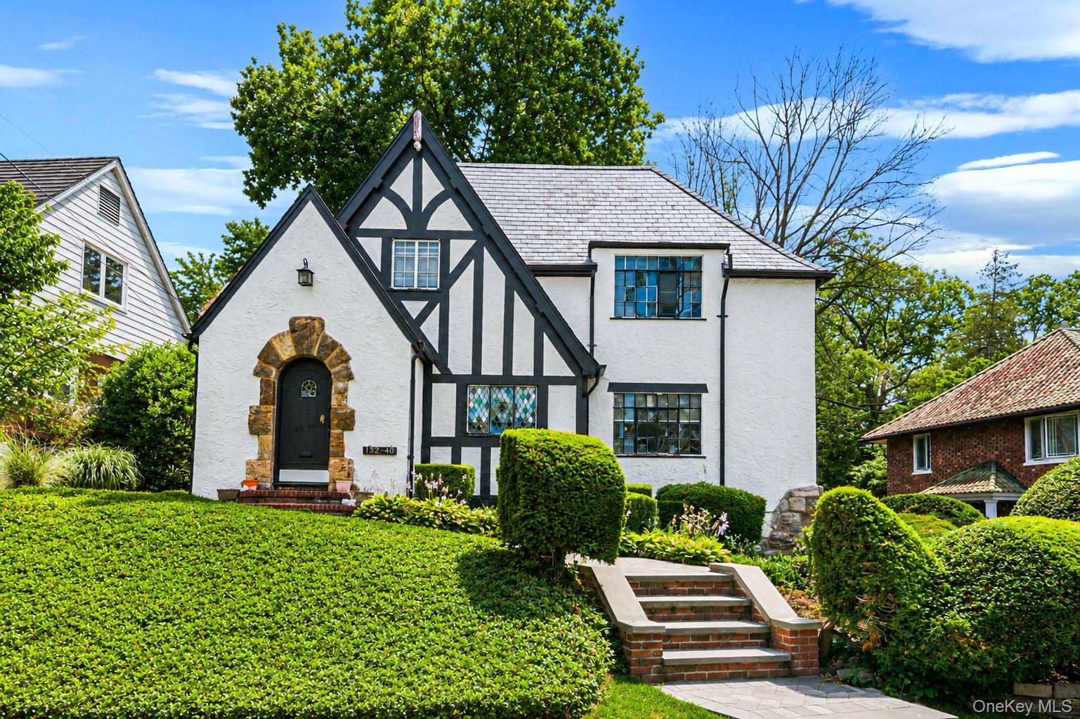 Tudor-style residence featuring a white stucco exterior with dark timber accents and a stone archway entrance