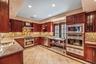 Kitchen featuring reddish brown cabinets, dark stone countertops, glass insert cabinets, appliances with stainless steel finishes, and wall chimney ra