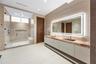 Spa-style primary bath with double floating vanity, book-matched red-veined stone countertop, backlit LED mirror, large-format travertine wall tiles,