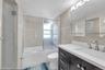 Bathroom featuring a dark wood-finish vanity with a white countertop and undermount sink, brushed nickel fixtures, a framed mirror cabinet, and tiled