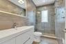 Modern bathroom featuring a white vanity with an integrated sink, a frameless lighted, anti fog mirror, and a glass-enclosed shower with porcelain til