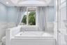 Deep soaking tub with polished chrome fixtures, surrounded by white wainscoting and light marble-finish tile